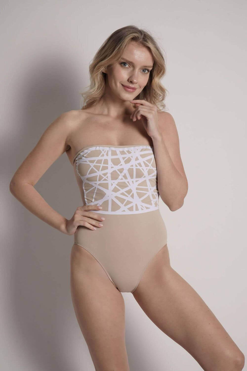 The Angela camel strapless one piece swimsuit features a geometric detail of laser-cut lycra in white. This exquisite design is permanently applied on the camel background.
